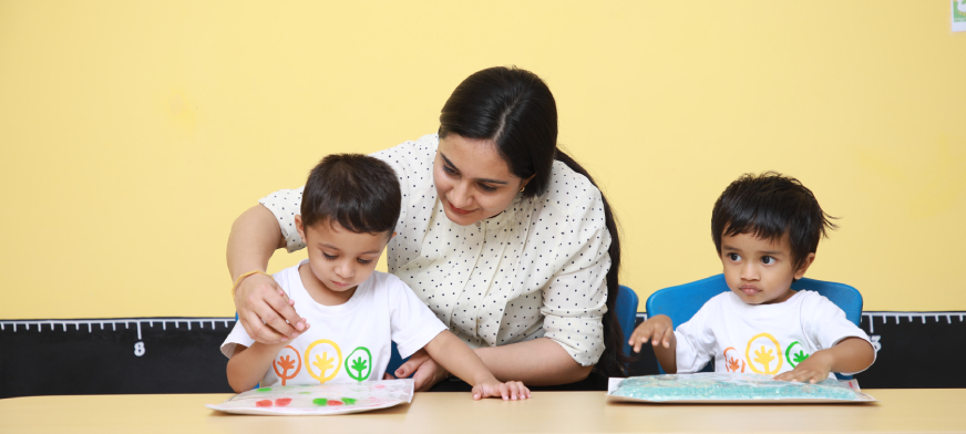 Teacher guiding two young children with creative activities at a preschool in Yelahanka.
                  